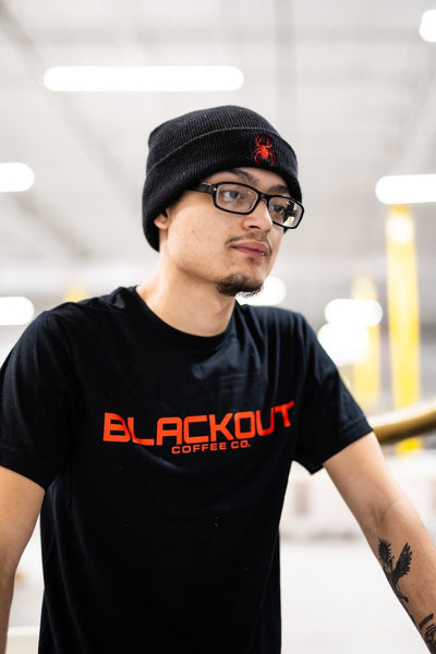 Person wearing a black t-shirt with 'Blackout Coffee Co.' text and a black beanie indoors.