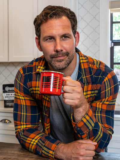 Man in a plaid shirt holding a red mug in a kitchen