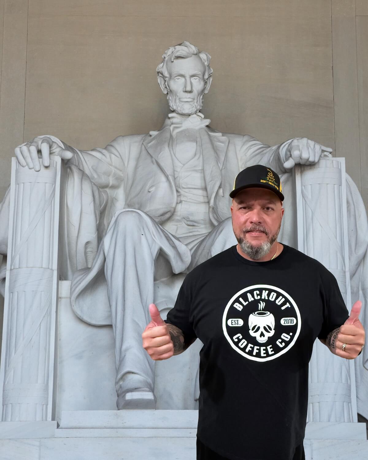 Jared Yanis from Guns & Gadgets wearing a Blackout Coffee Co. t-shirt in front of a statue