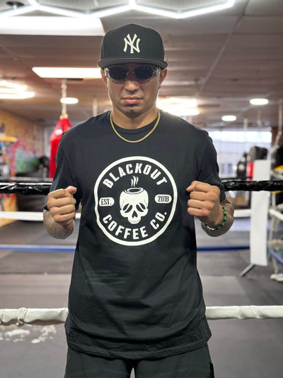 Person wearing a black t-shirt with 'Blackout Coffee Co.' logo in a gym setting