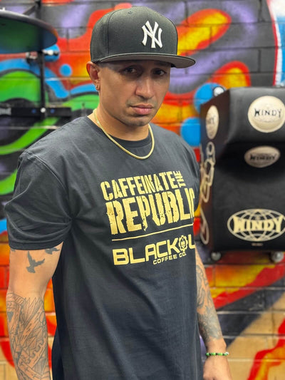 Man wearing a black t-shirt with yellow text and a cap, standing in front of a colorful mural.