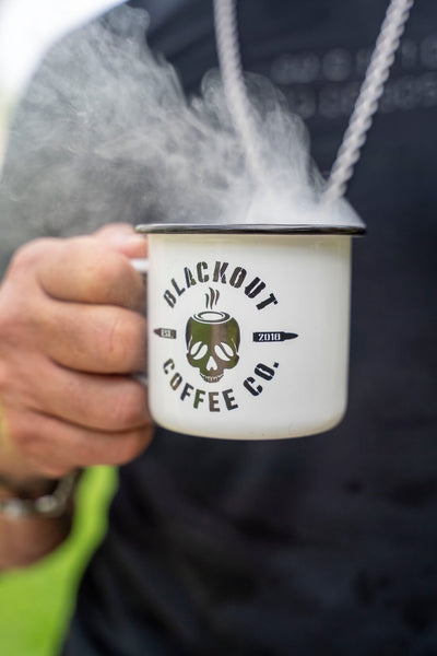 Person holding a 'Blackout Coffee Co.' mug with steam rising from it.