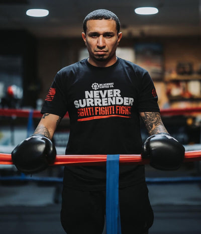 Person wearing a black t-shirt with 'Never Surrender Fight Fight Fight' text, holding boxing gloves in a gym.