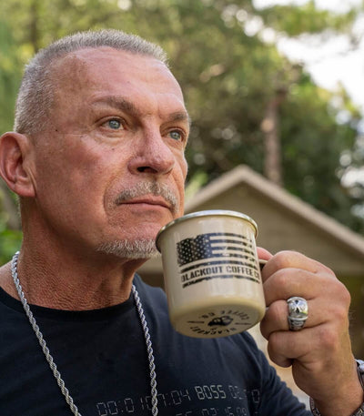 Man holding a 'Blackout Coffee' mug outdoors with trees in the background
