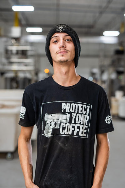 Person wearing a black t-shirt with 'Protect Your Coffee' graphic in a warehouse setting
