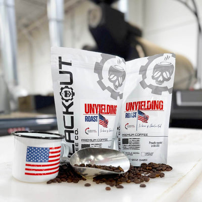 Two bags of 'Unyielding Roast' coffee with a mug in front of roaster.
